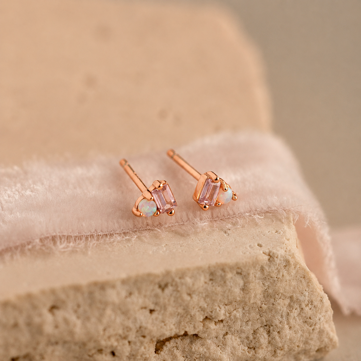 Rose gold earrings with gemstones on a soft fabric background